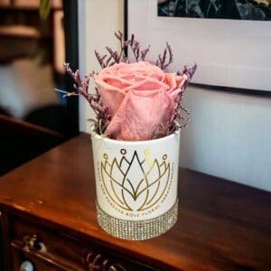 A pink rose in a white vase on top of a table.