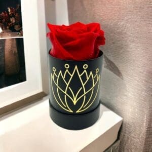 A red rose in a black vase on top of a table.