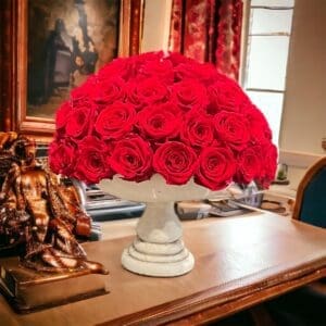 A white vase with red roses on top of it.