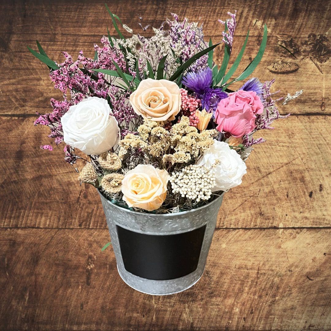 A bucket of flowers on top of a wooden table.